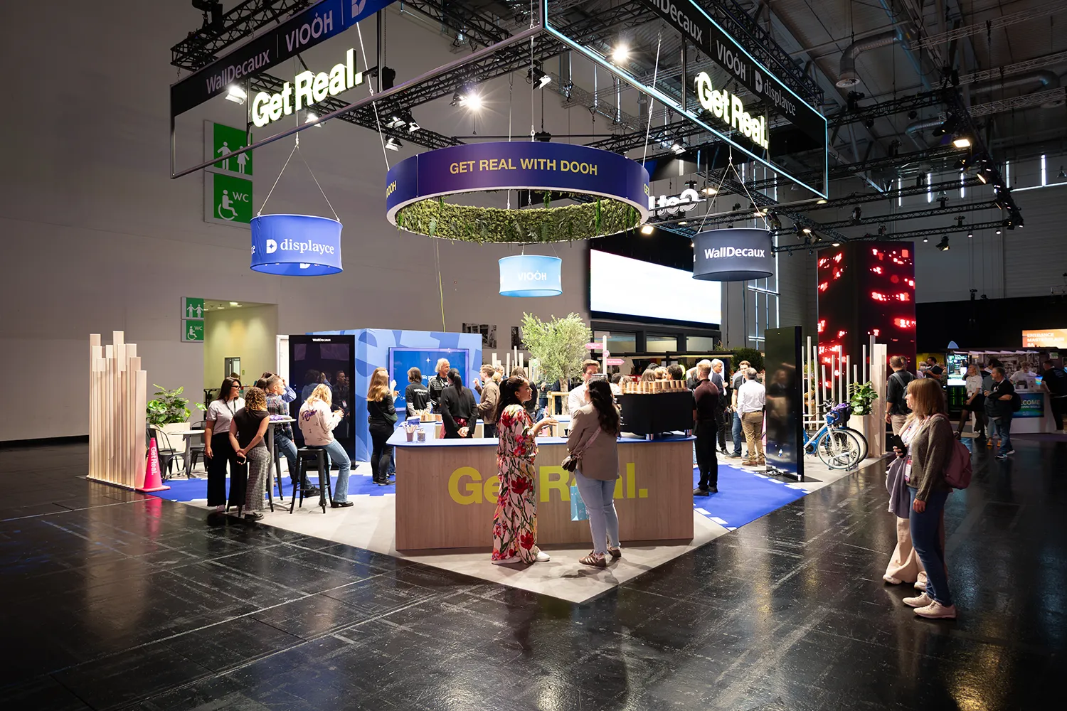 Offener WallDecaux-Stand mit Besuchergruppen und Branding „Get Real“.