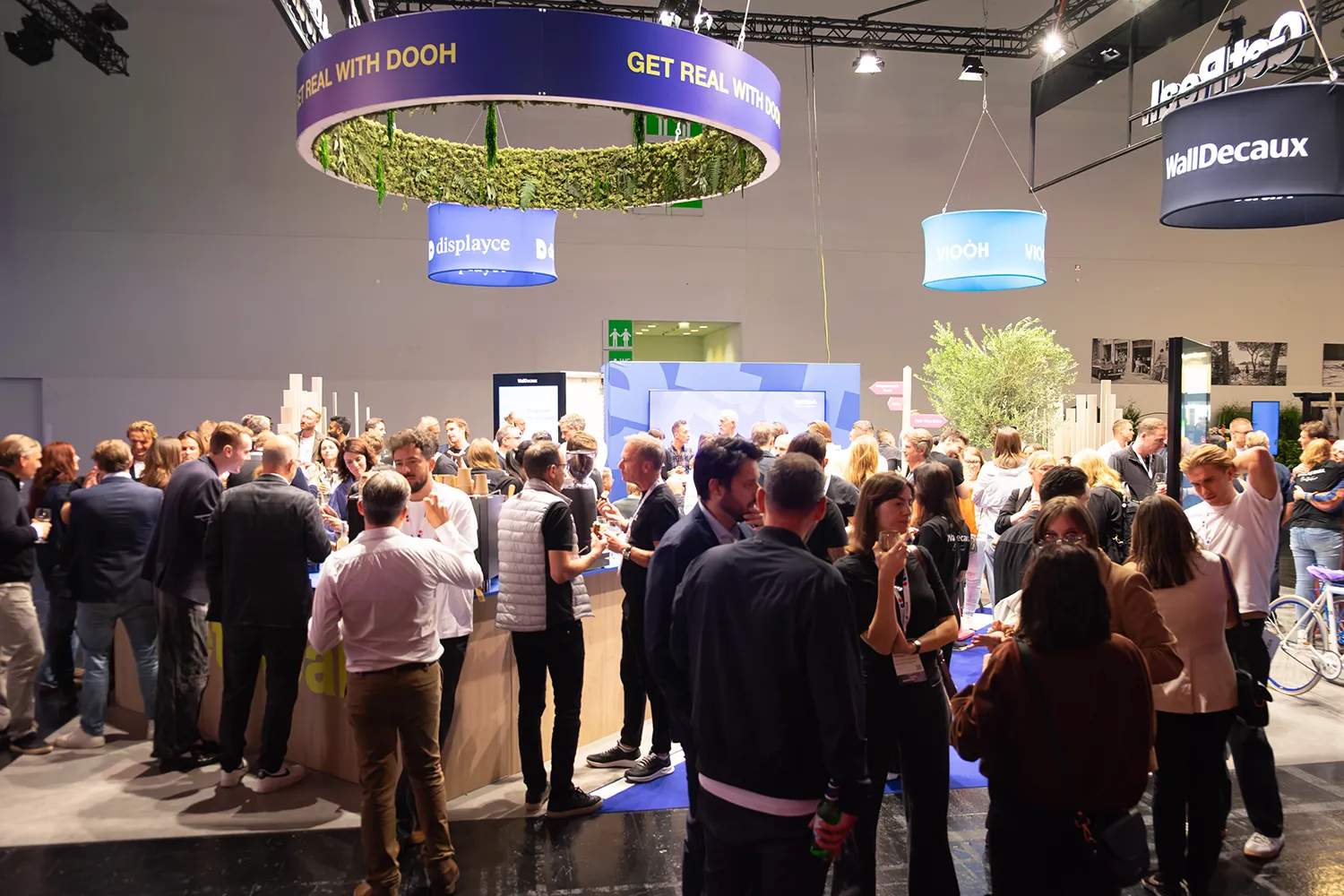 Offener WallDecaux-Stand mit großer Besuchergruppe und Branding „Get Real"