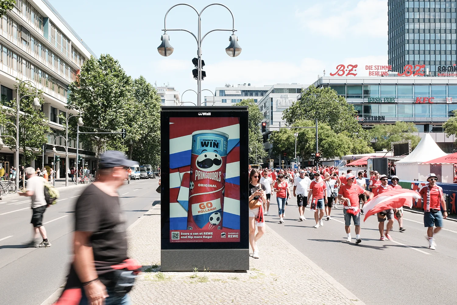 Digital City Light Poster am Breitscheidplatz Berlin mit Chips-Werbung, umgeben von Fussball-Fans.