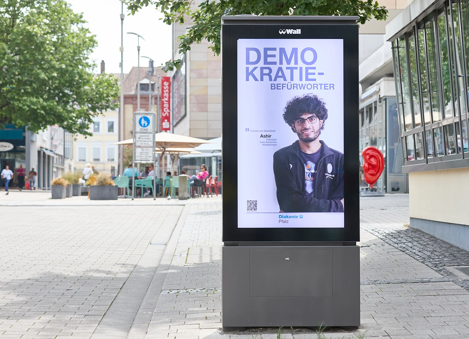 Digital City Light Poster in Fußgängerzone zeigt Kampagne zur Demokratie.
