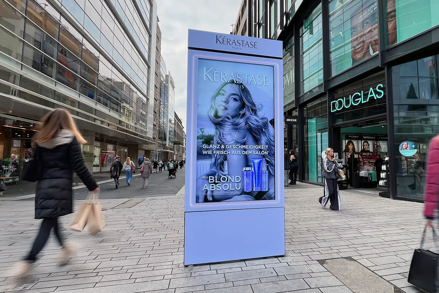 Digital advertising screen showing a woman for KERASTASE, on a busy city street.