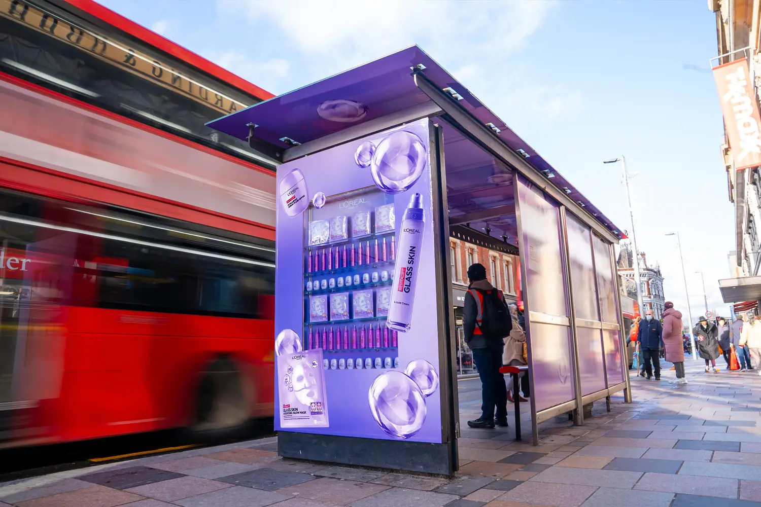 Bus stop with a digital ad for purple products, red bus passing with motion blur.