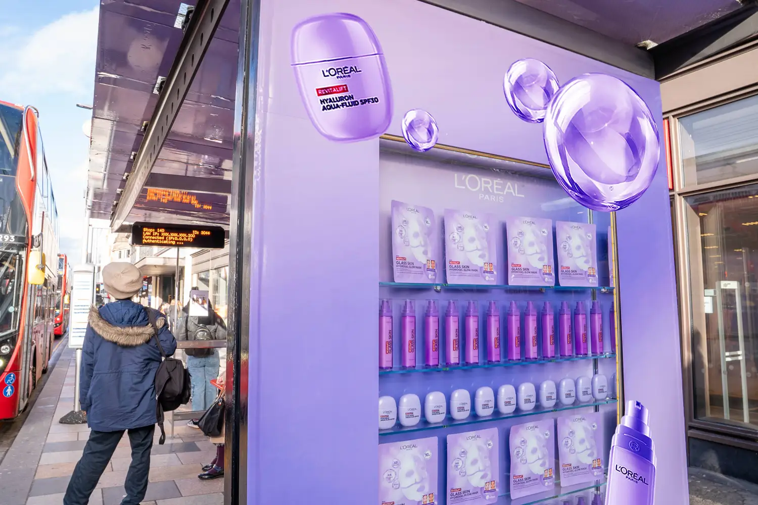 Man views a large L'Oréal 'Glass Skin' product display next to a red bus.