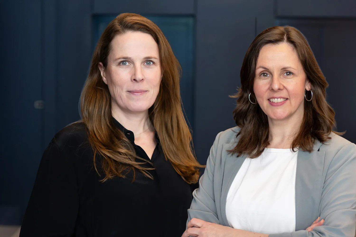 Two professional women with brown hair posing for a headshot in an office setting.