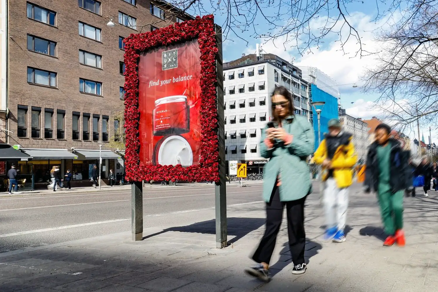 Red floral-framed Rituals billboard for beauty products with "find your balance" on a city street.