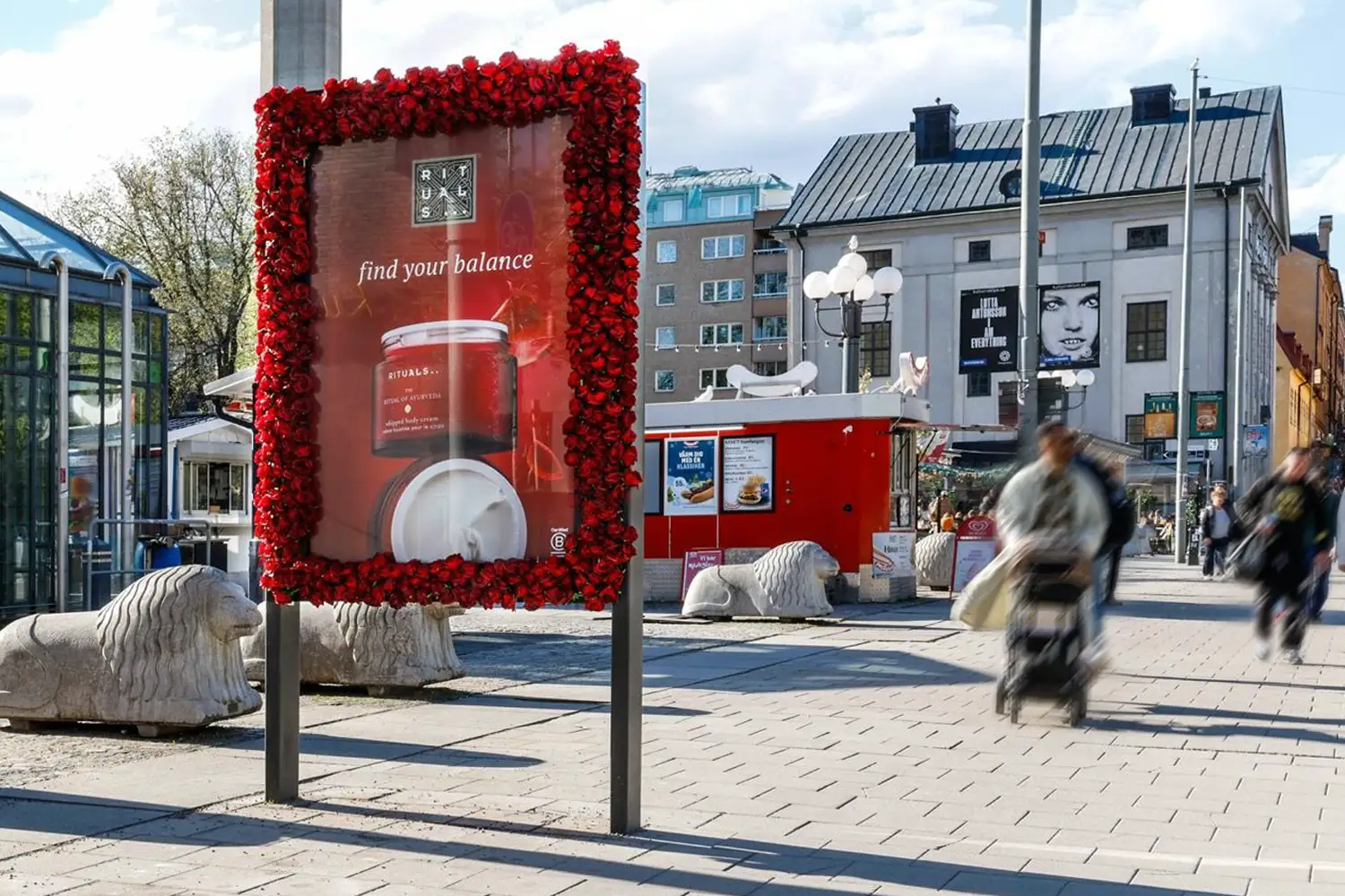 Red floral-framed Rituals billboard showing beauty products and "find your balance" text in a city.