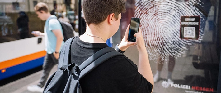 Person an einer Buswartehalle interagiert mit Recruiting-Kampagne durch das Scannen eines QR-Codes auf einem City Light Poster.