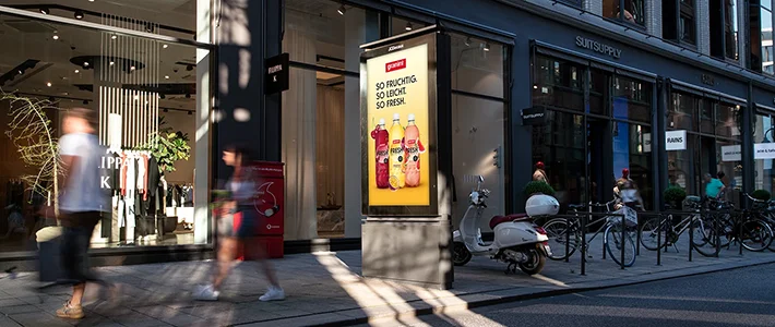 Digital City Light Poster zeigt Getränkewerbung in Einkaufsstraße im Sommer.