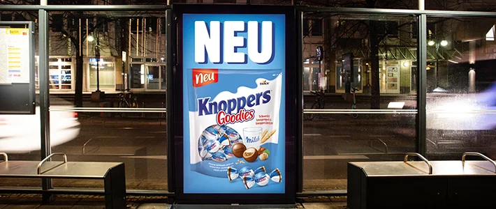 Digital City Light Poster mit Süßwarenwerbung in Tramwartehalle in Berlin bei Nacht.