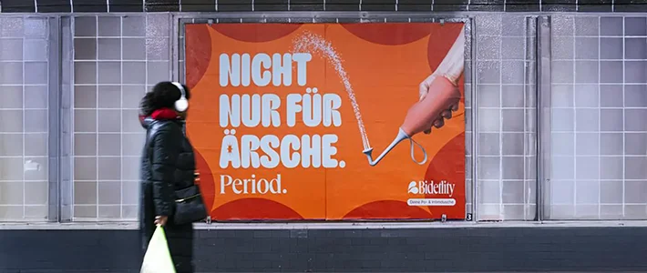 Großes Plakat hinter U-Bahn-Gleis mit Werbung für Hygieneartikel in Berlin. Eine Frau steht im Vordergrund und betrachtet das Plakat.