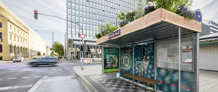 City Light Poster und vollbeklebte Bus-Wartehalle mit Gründach zeigen Werbung für Tiernahrung.